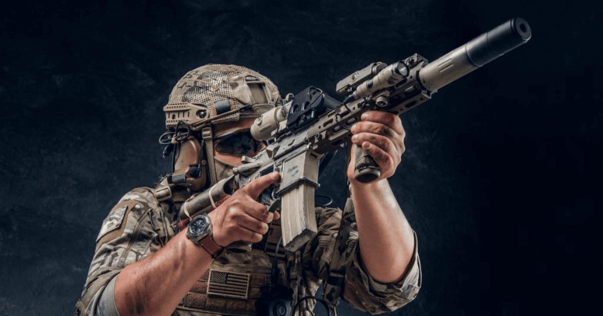 Atirador com roupa tática usa um fuzil equipado com mira e silenciador.