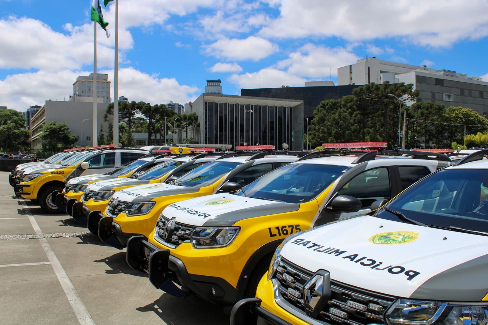 Fileira de viaturas policiais estacionadas diante de prédio público do Paraná.