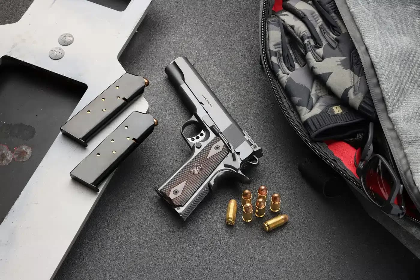 Pistola Springfield Armory 1911, carregadores e munição sobre bancada.