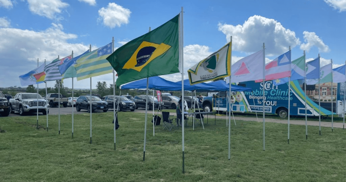 Bandeiras de vários países alinhadas em área externa de competição de tiro.