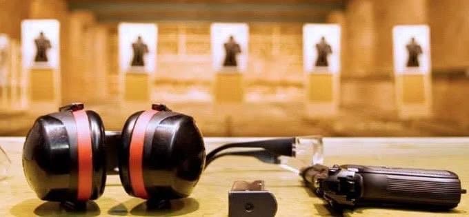 Abafadores, pistola e alvo de papel sobre bancada de estande de tiro.