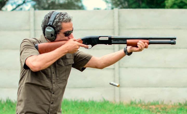 Homem dispara uma espingarda em um campo de tiro ao ar livre.