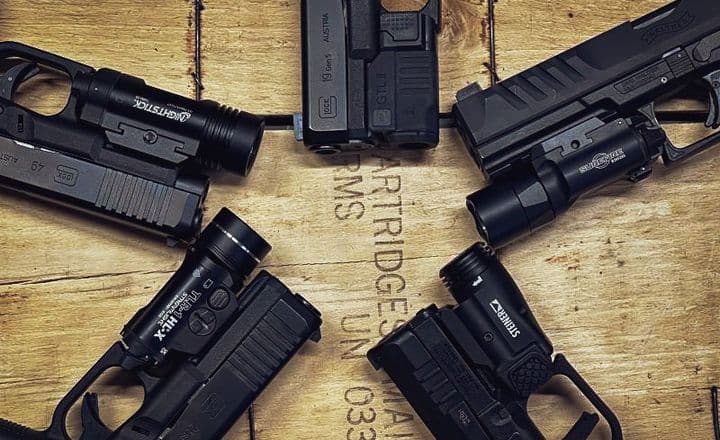 Quatro pistolas equipadas com lanternas sobre uma caixa de madeira.