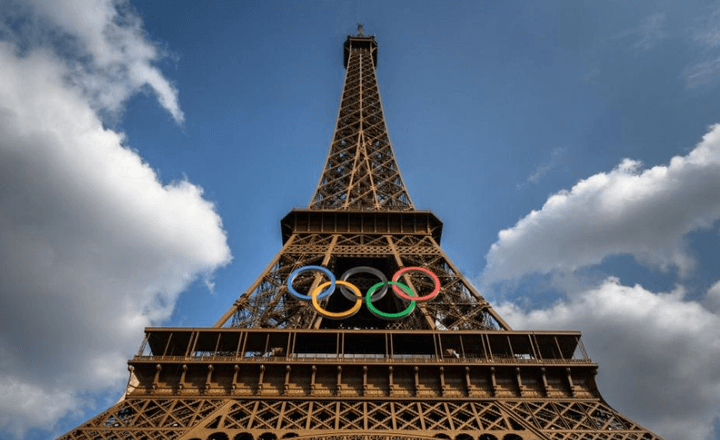 Torre Eiffel decorada com os anéis olímpicos sob céu azul.