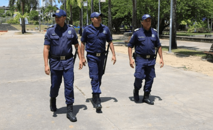 Três guardas municipais caminham em uma praça pública do Recife.
