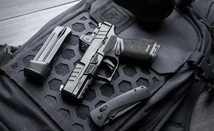 Pistola, carregador e canivete apoiados sobre uma bolsa tática preta.