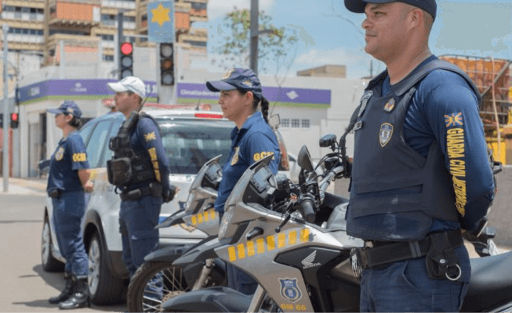 Guardas civis municipais trabalham junto a motocicletas em uma via urbana.
