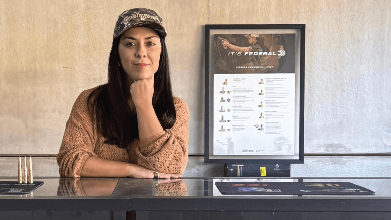 Mulher posa em balcão da Hunterr diante de quadro com componentes de munição.