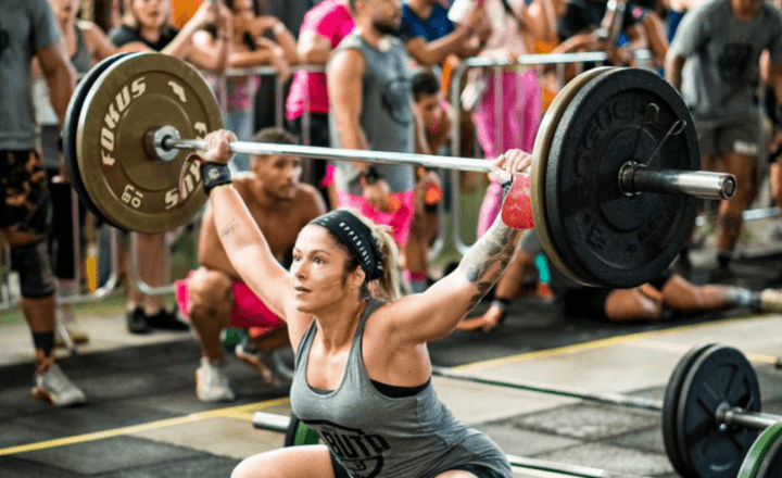Atleta feminina levanta uma barra com pesos em competição de crossfit.