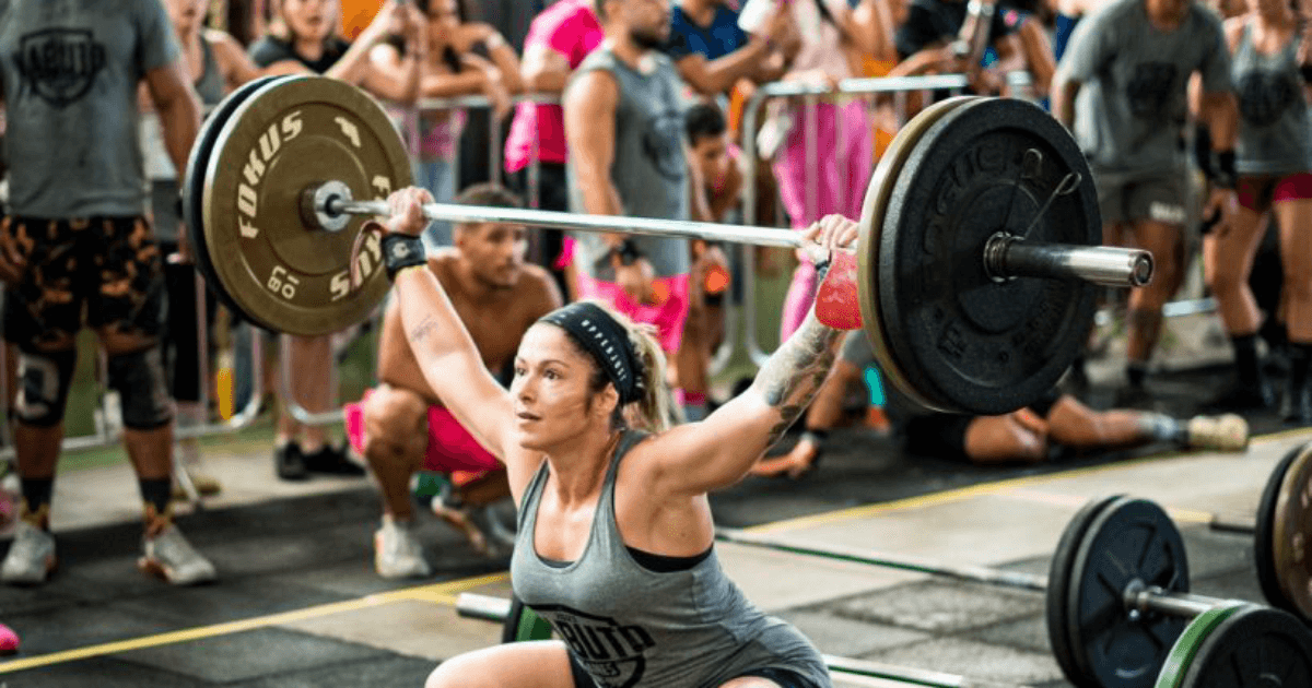 Atleta feminina levanta uma barra com pesos em competição de crossfit.