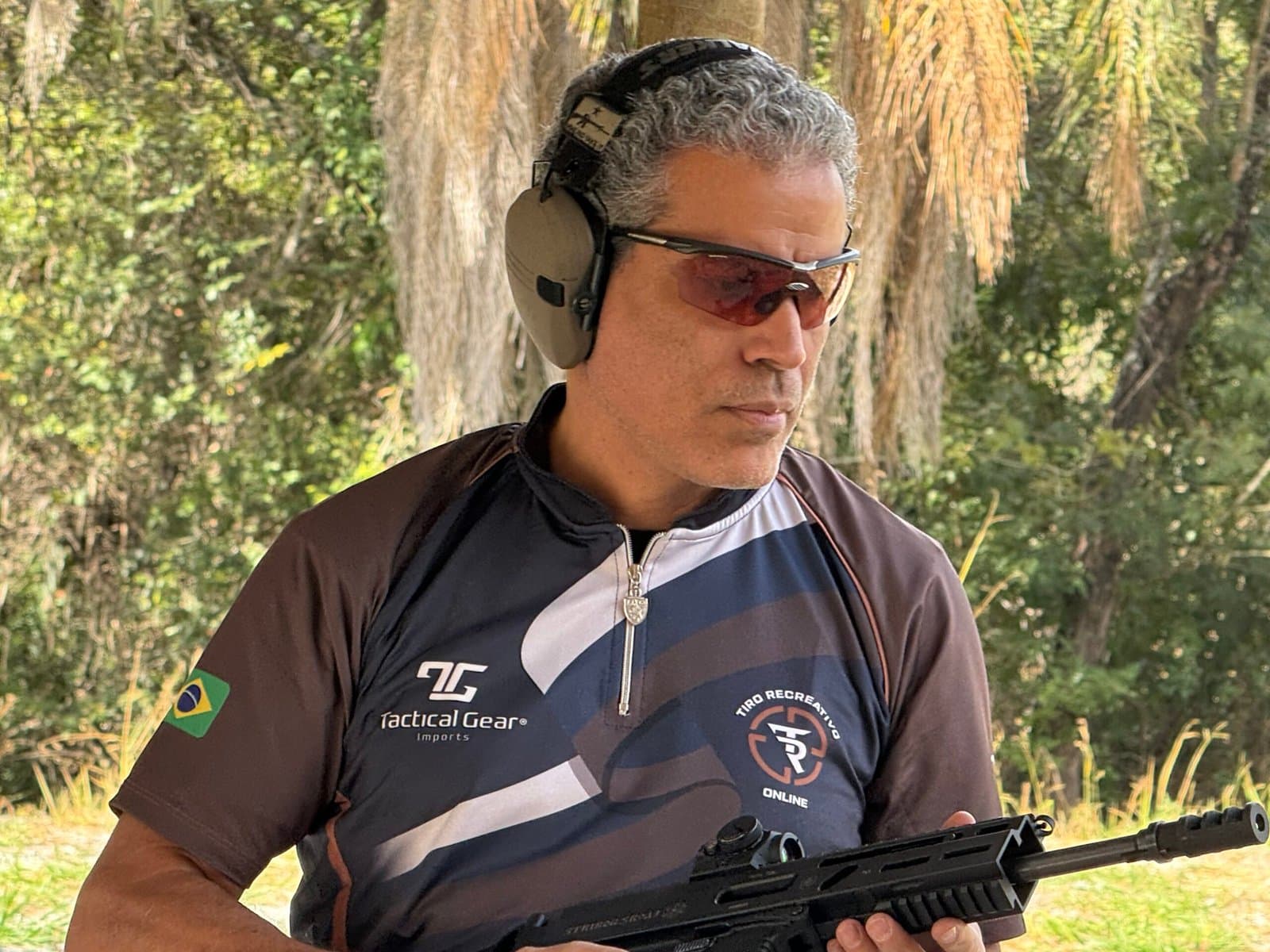 Demetrius Oliveira em campo de tiro com uniforme e equipamento de proteção.