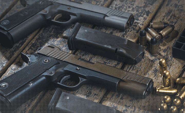 Duas pistolas, carregadores e cartuchos sobre uma bancada de madeira.