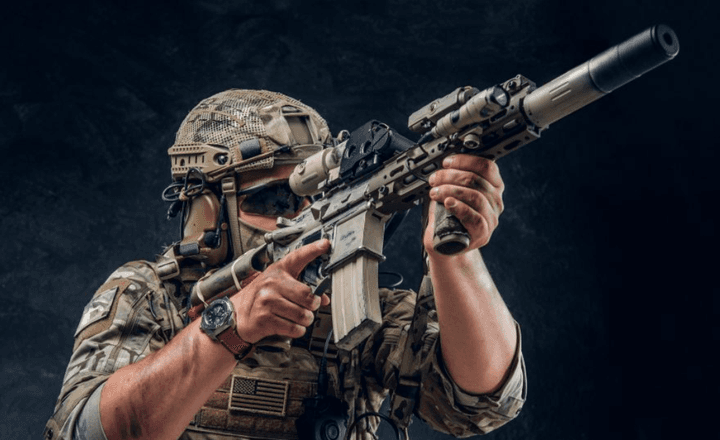 Atirador com roupa tática usa um fuzil equipado com mira e silenciador.