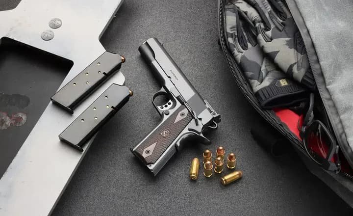 Pistola Springfield Armory 1911, carregadores e munição sobre bancada.