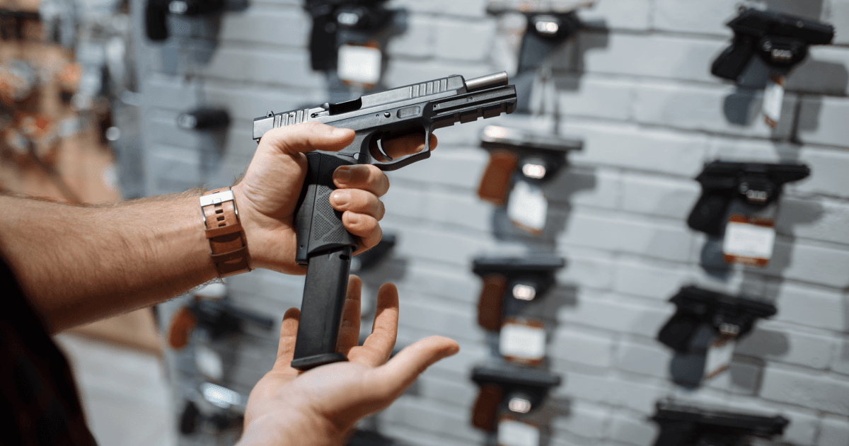 Pessoa segura uma pistola com carregador alongado dentro de uma loja de armas.