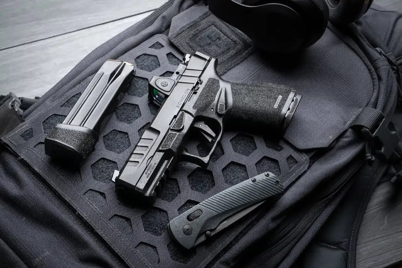 Pistola, carregador e canivete apoiados sobre uma bolsa tática preta.