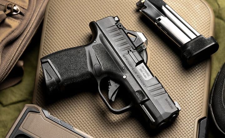 Pistola Springfield Armory Hellcat, carregador e celular sobre bolsa tática.