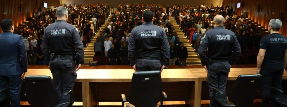Policiais penais diante de auditório lotado durante cerimônia.
