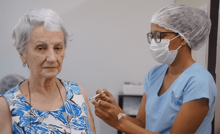Profissional de saúde aplica vacina no braço de uma mulher idosa.