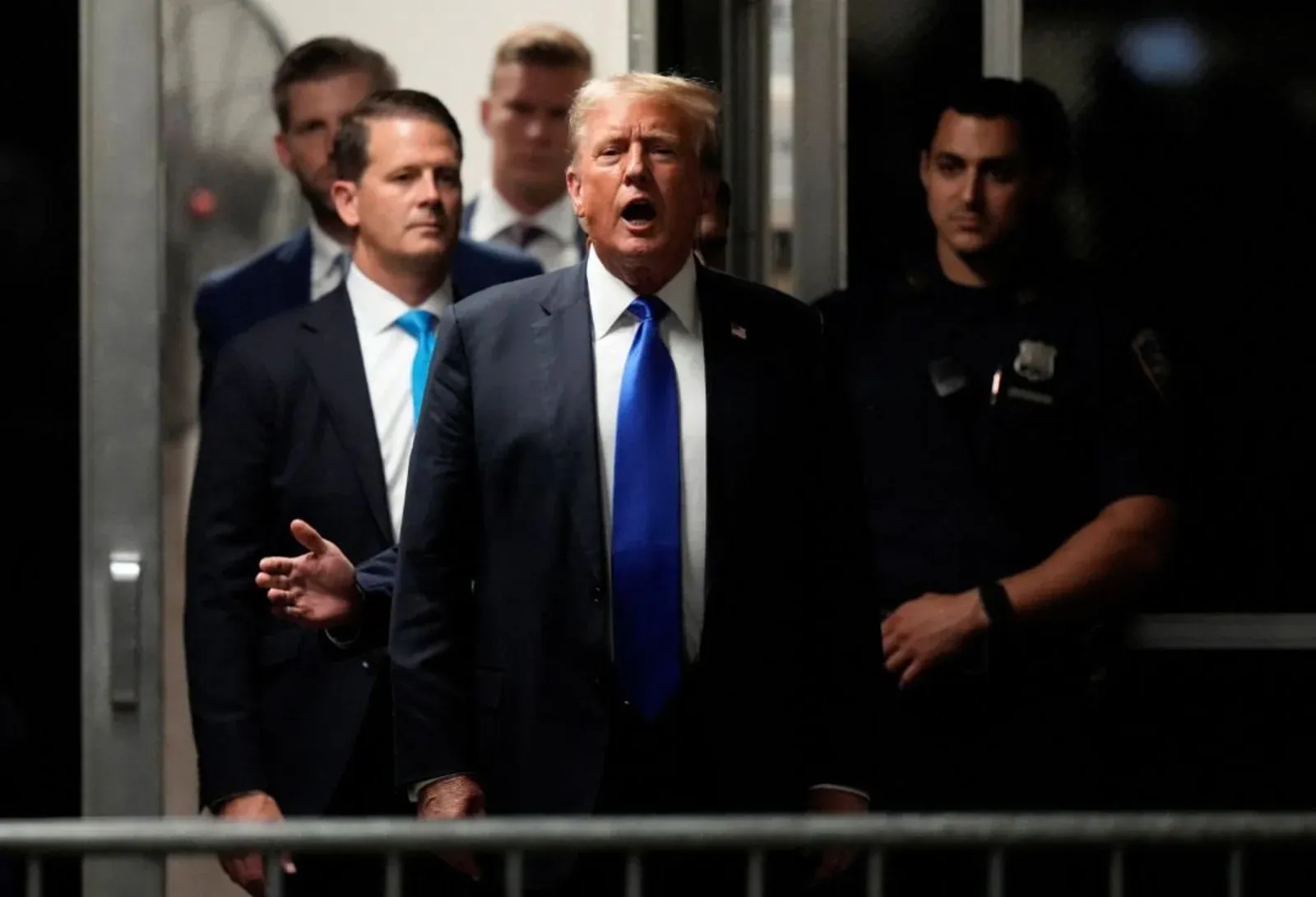 Donald Trump fala a jornalistas ao sair de um edifício acompanhado por assessores.