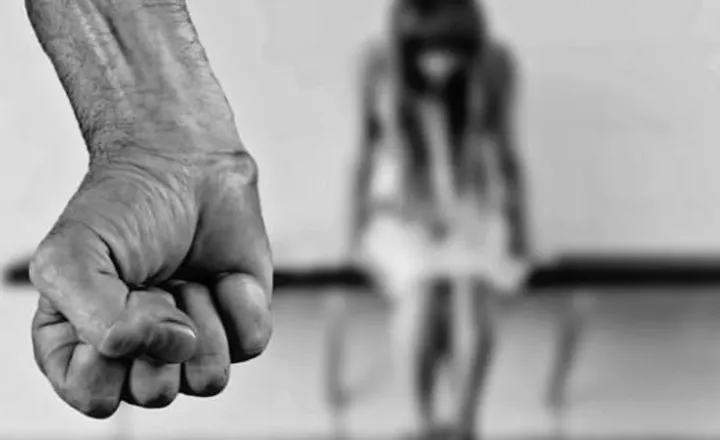 Punho fechado em primeiro plano e silhueta desfocada de adolescente ao fundo.