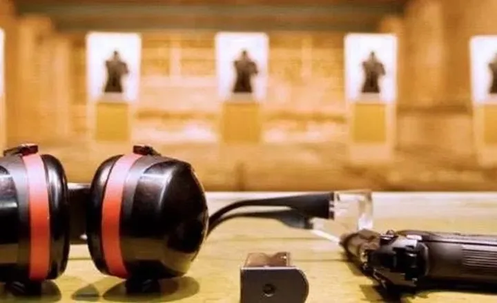 Abafadores, pistola e alvo de papel sobre bancada de estande de tiro.