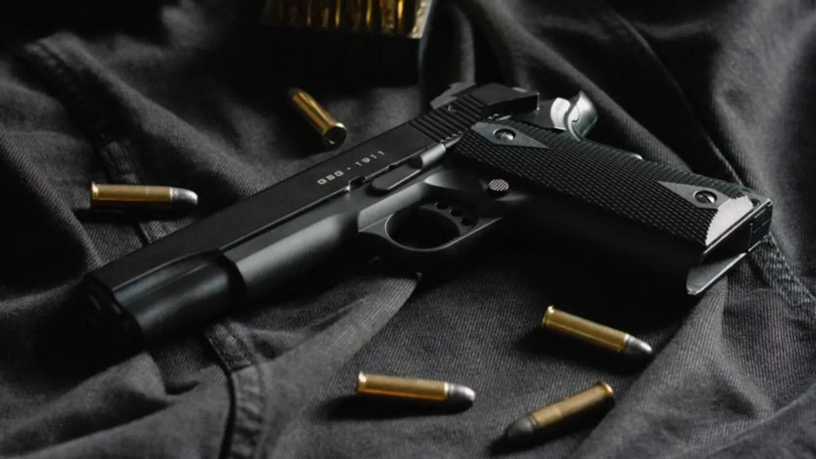 Pistola preta e cartuchos sobre tecido escuro.