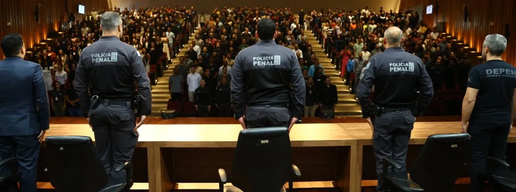 Policiais penais diante de auditório lotado durante cerimônia.