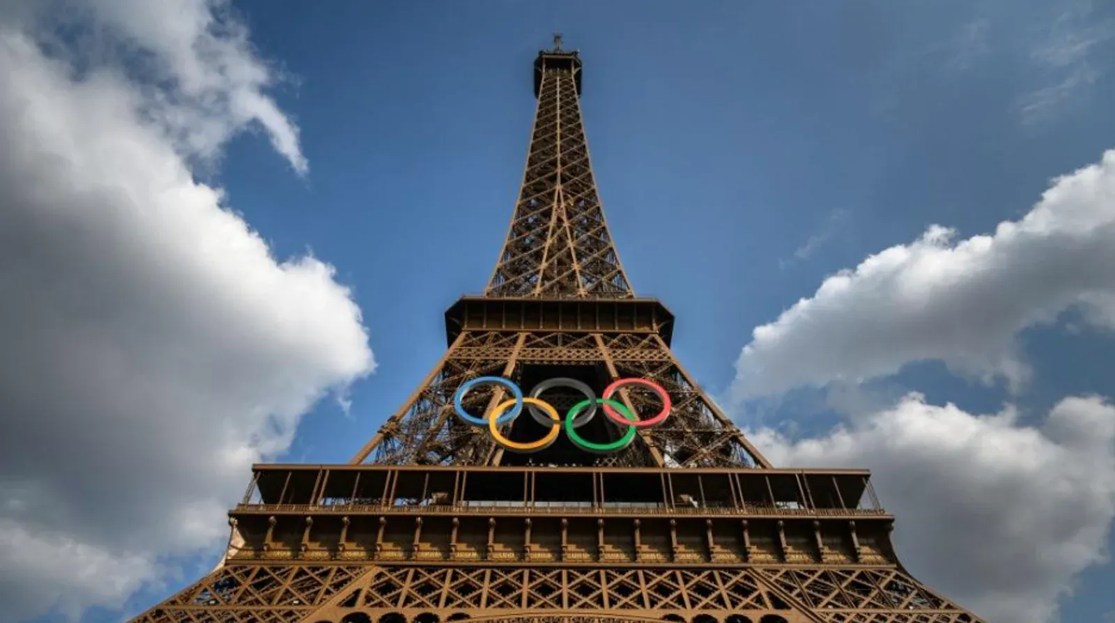 Torre Eiffel decorada com os anéis olímpicos sob céu azul.