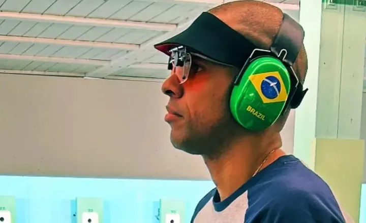 Atirador brasileiro usa óculos e abafador com bandeira do Brasil.