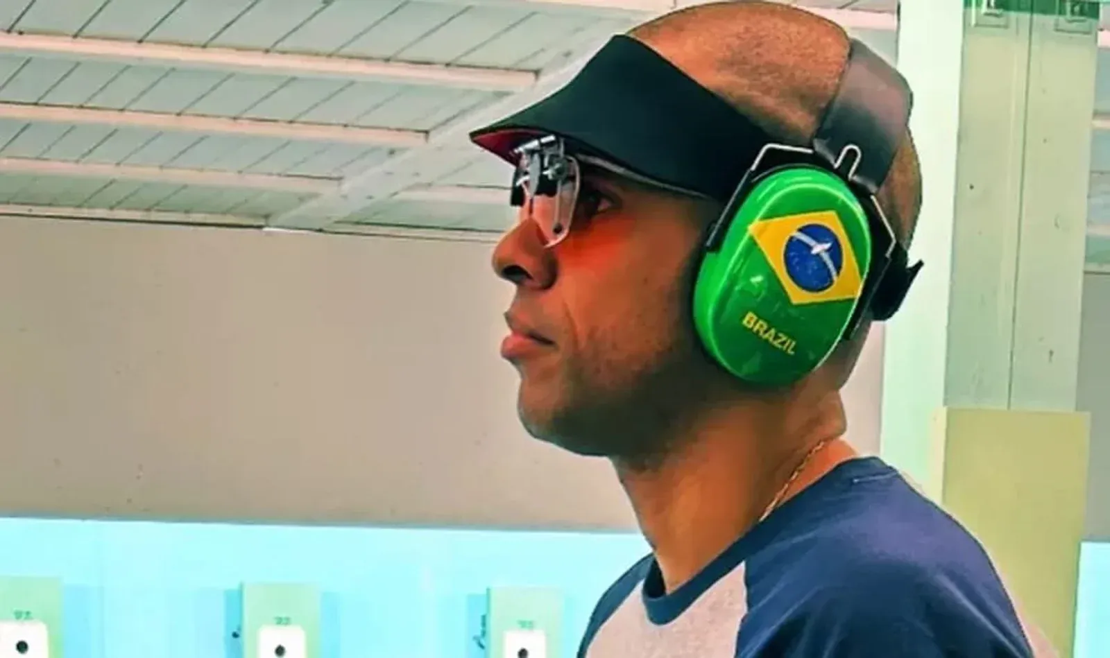 Atirador brasileiro usa óculos e abafador com bandeira do Brasil.