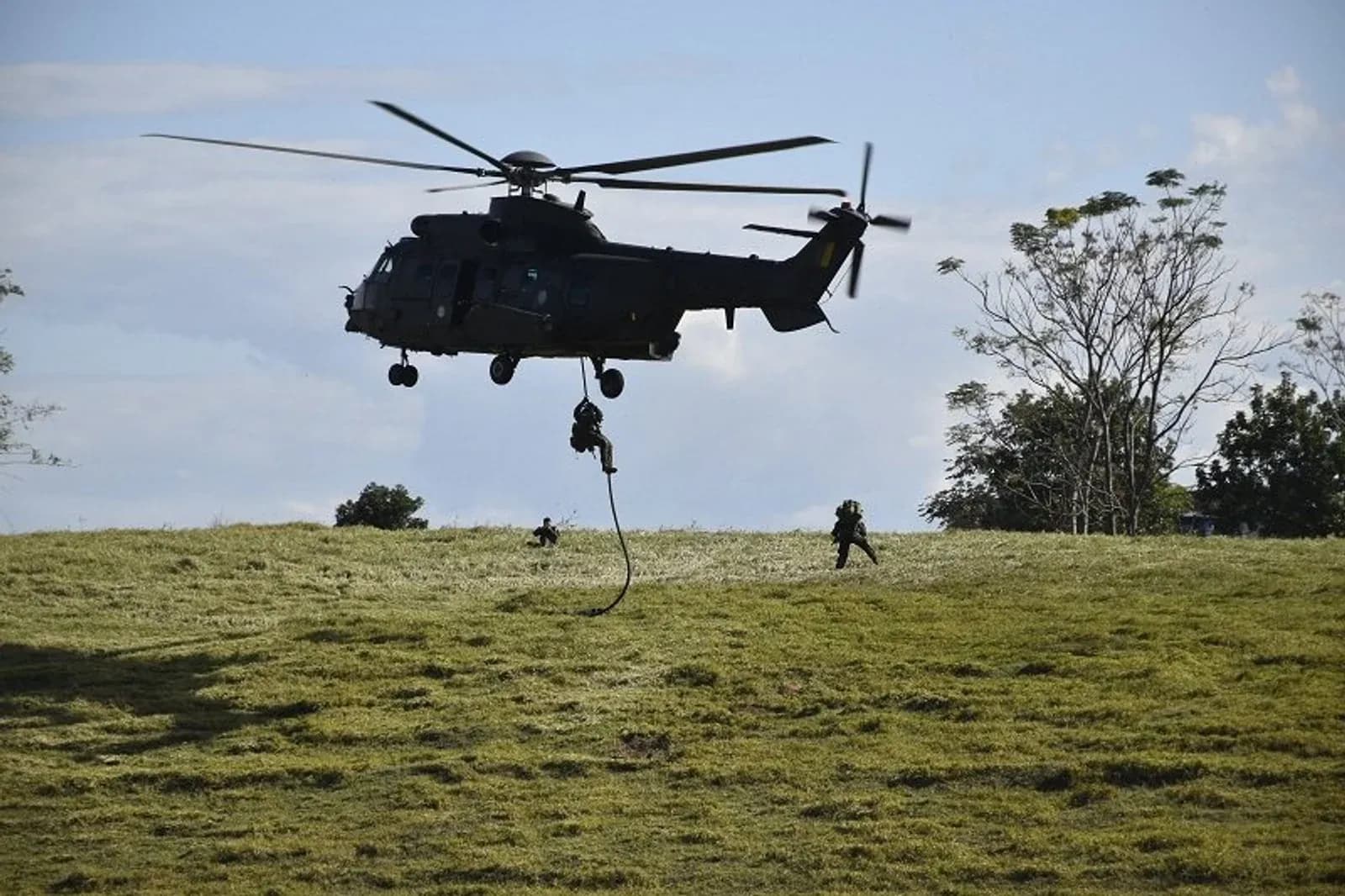 Militar desce por corda de helicóptero durante treinamento em campo.