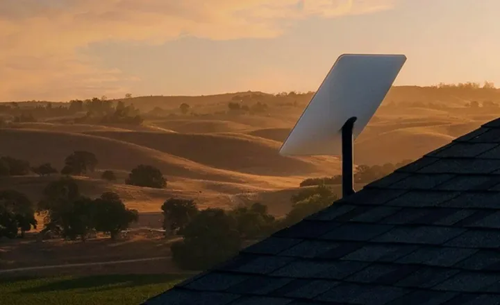Antena Starlink instalada em telhado diante de paisagem rural ao pôr do sol.