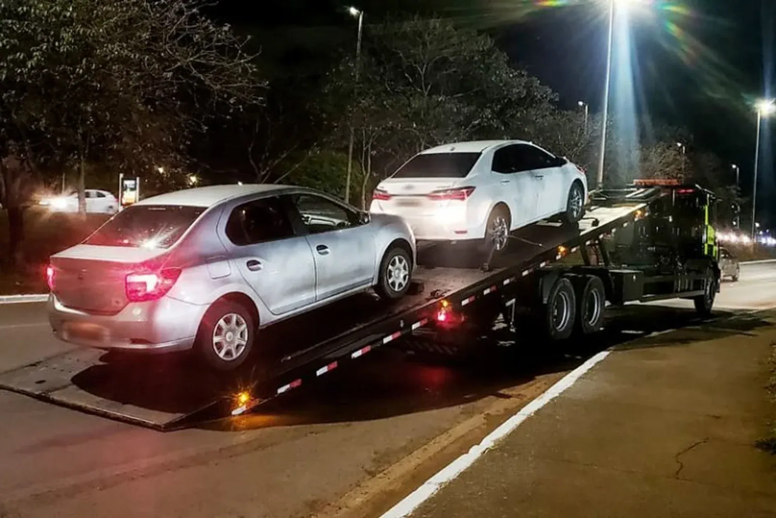 Automóveis são transportados por caminhão-guincho durante a noite.