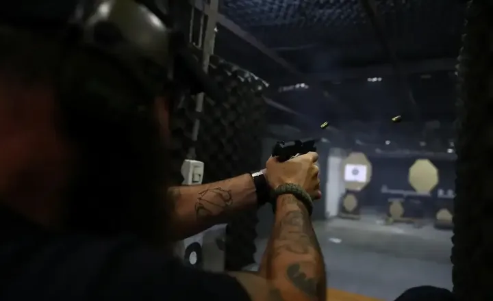 Pessoa dispara uma pistola em um estande de tiro escuro.
