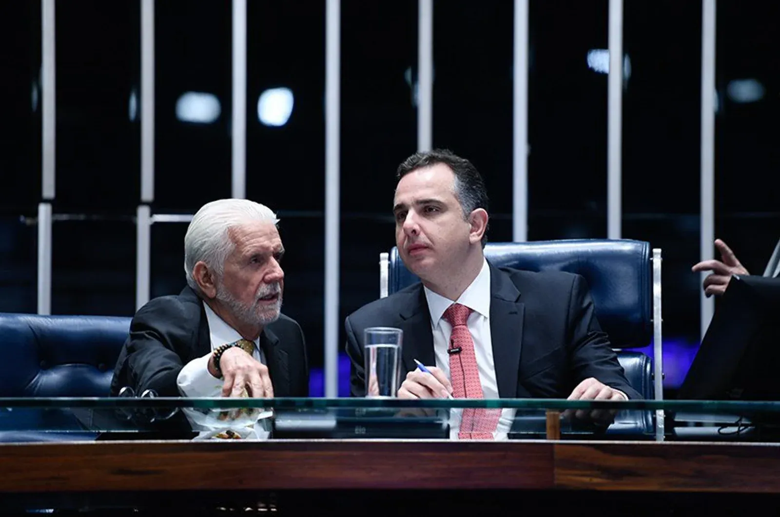 Dois senadores conversam à mesa diretora do plenário.