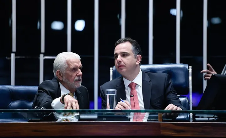Dois senadores conversam à mesa diretora do plenário.
