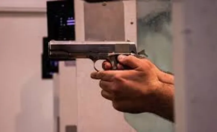 Pessoa segura uma pistola em um estande de tiro.