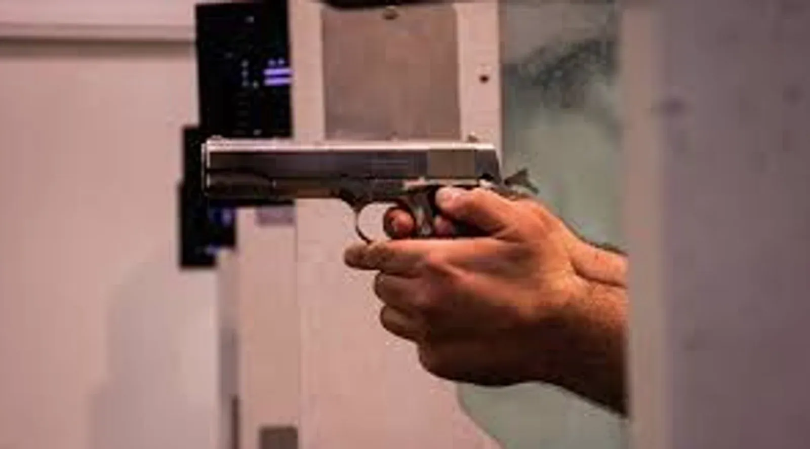 Pessoa segura uma pistola em um estande de tiro.