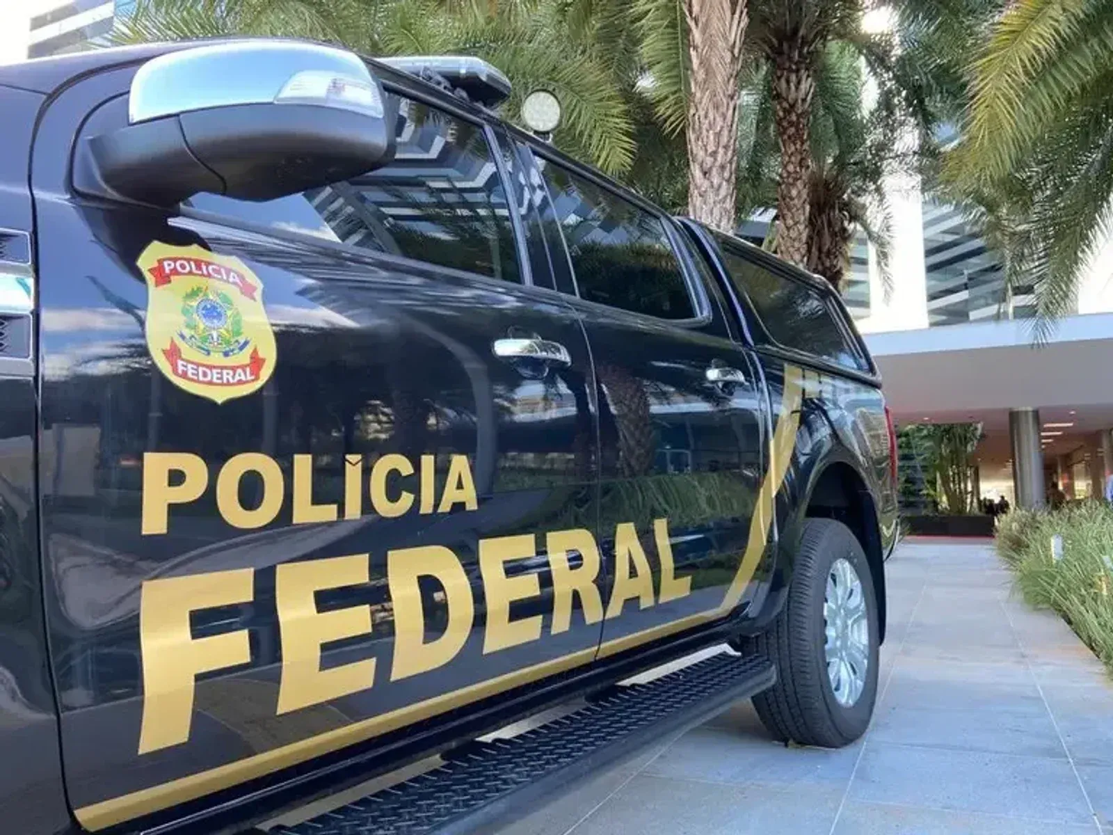 Viatura da Polícia Federal estacionada diante de edifício.