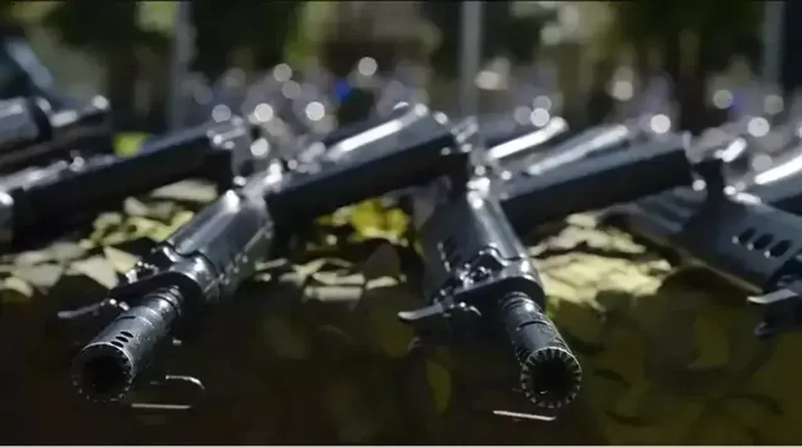 Fuzis alinhados sobre tecido camuflado.
