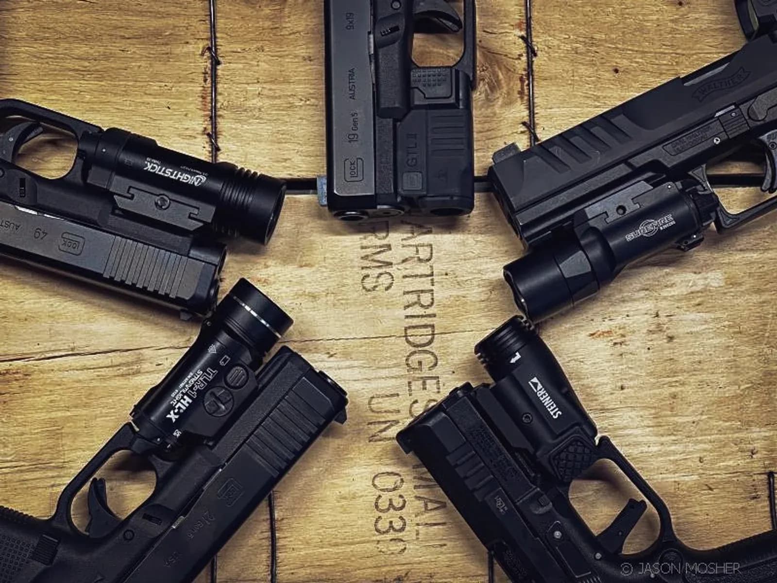 Quatro pistolas equipadas com lanternas sobre uma caixa de madeira.