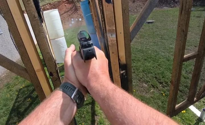 Atirador aponta uma pistola equipada com mira em uma pista de competição.