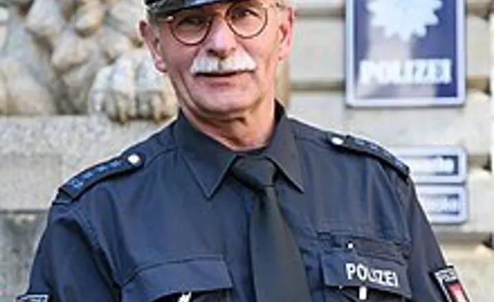 Policial alemão uniformizado segura um rádio diante de uma delegacia.