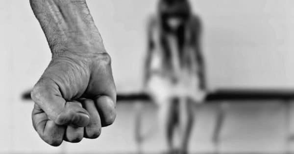 Punho fechado em primeiro plano e silhueta desfocada de adolescente ao fundo.