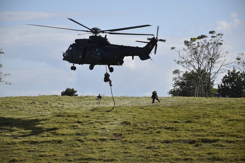 Militar desce por corda de helicóptero durante treinamento em campo.